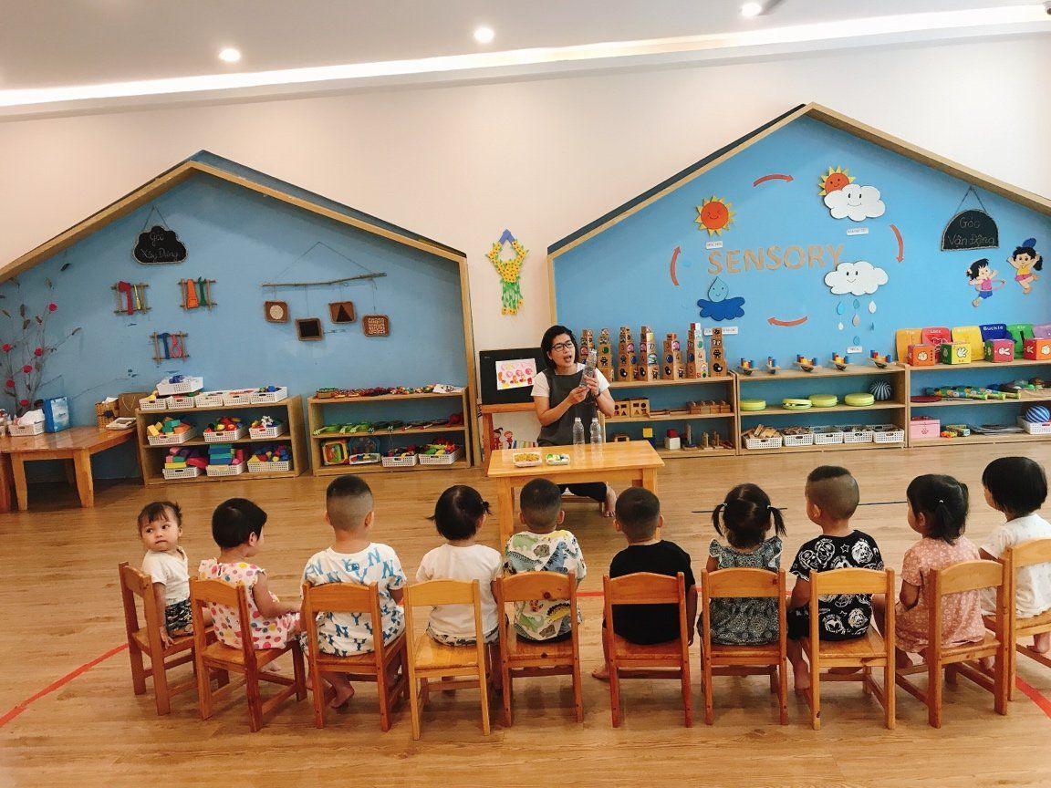 Cô giáo giới thiệu giáo cụ ở góc Sensory, các bé ngồi thành hàng