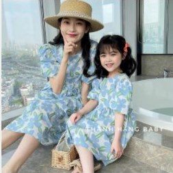 Mẹ và bé gái mặc váy hoa chanh xanh giống nhau, đội mũ cói